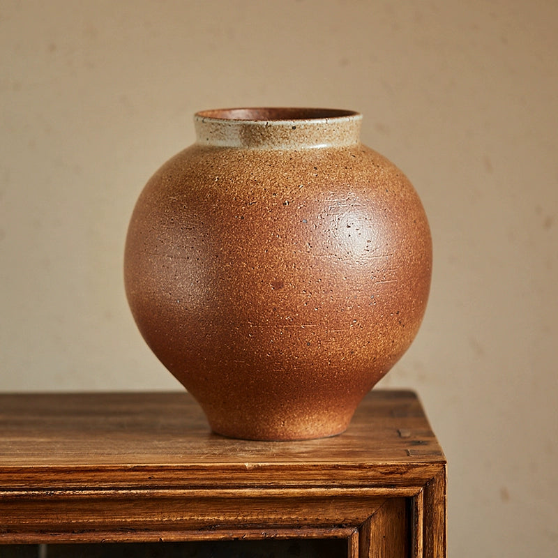 Rustic brown handmade pottery vase with a unique textured glaze.  Light beige highlights around the rim.  On a wooden surface.