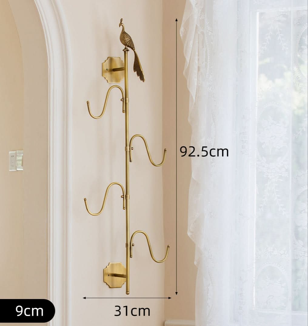 Vintage brass bird branch wall hooks with decorative hooks on a cream wall next to white lace curtains.