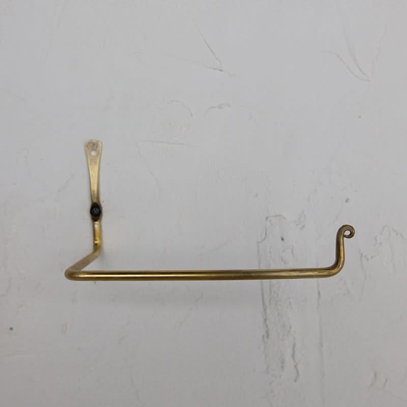 Gold toilet paper holder mounted on a textured white wall.