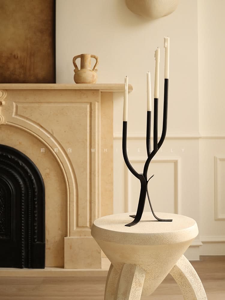 Modern Branch Candle Holder in black metal with white candles, set on a textured stool near a fireplace.