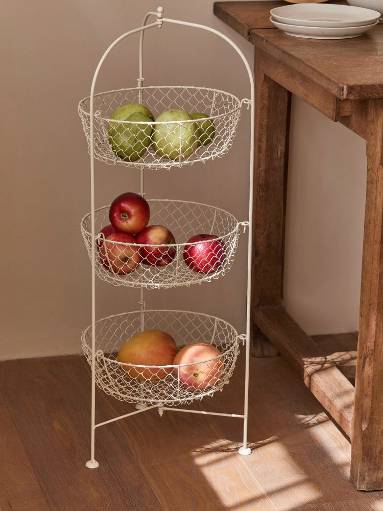 White wire fruit basket stand with 3 tiers.  Fresh produce in wire baskets. Rustic design.