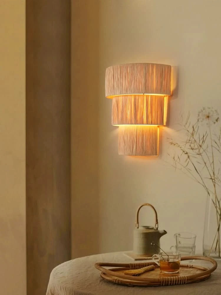 Natural raffia wall sconce light with three woven shades, providing warm ambient light.