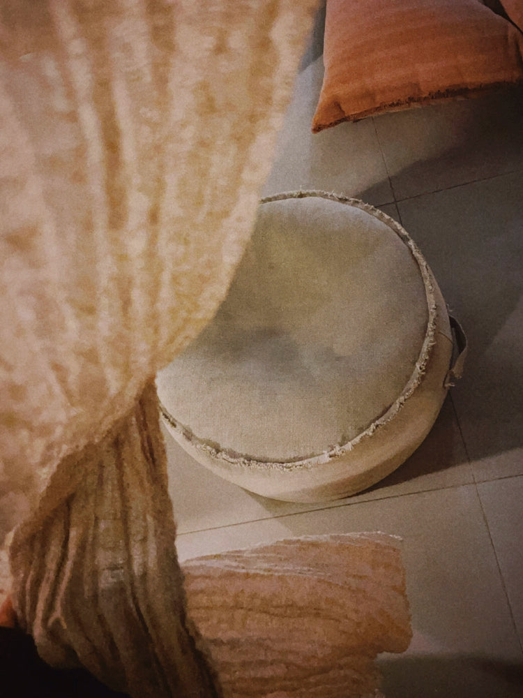 Round beige fabric ottoman pouf with decorative texture, accent seating for living room or bedroom.