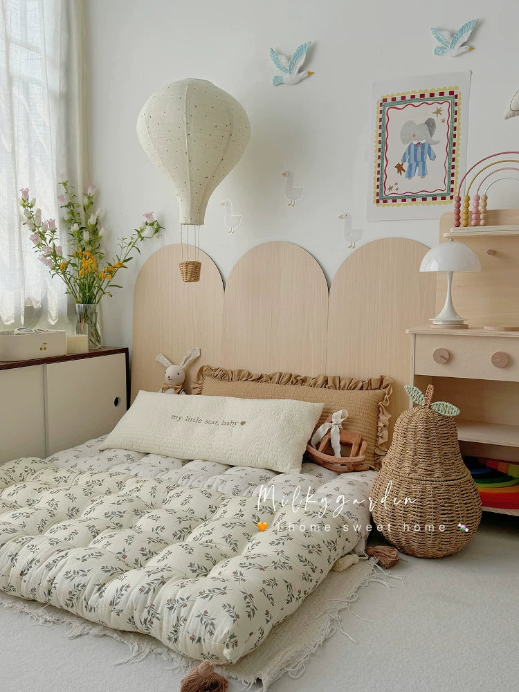 Quilted floor mattress with gray-green botanical print, decorative pillows, and nursery accents.