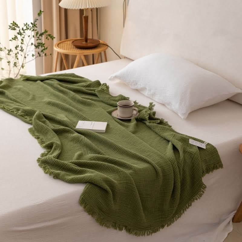 Green Four-Layer Waffle Weave Cotton Throw Blanket with tassels on a bed.