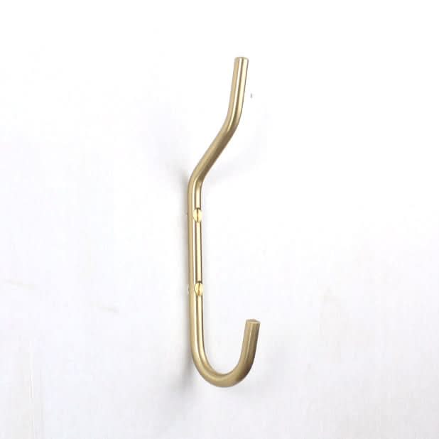 Minimalist brass wall hook with curved design, mounted on a white wall.