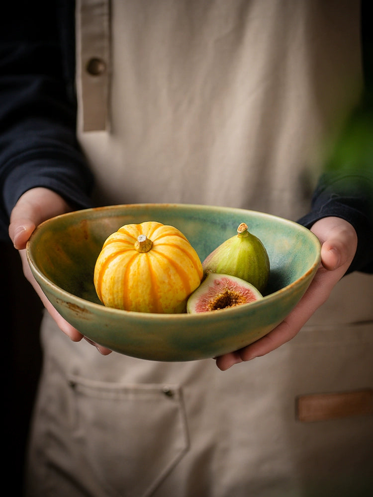 Hand-painted ceramic bowl with rustic green glaze holds a small gourd and figs.