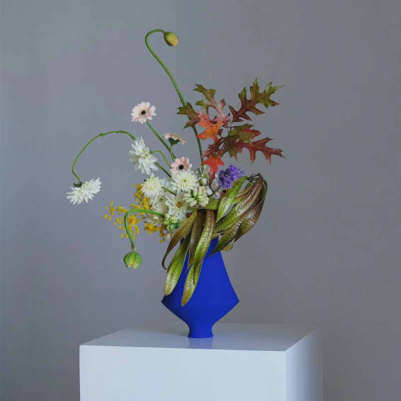 Klein Blue Flower Vase - Handcrafted ceramic vase with a vibrant floral arrangement on a white pedestal.