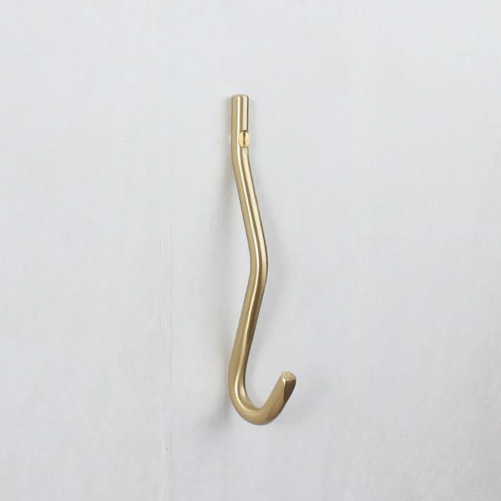 Minimalist brass wall hook with a modern, curved design, attached to a white wall.