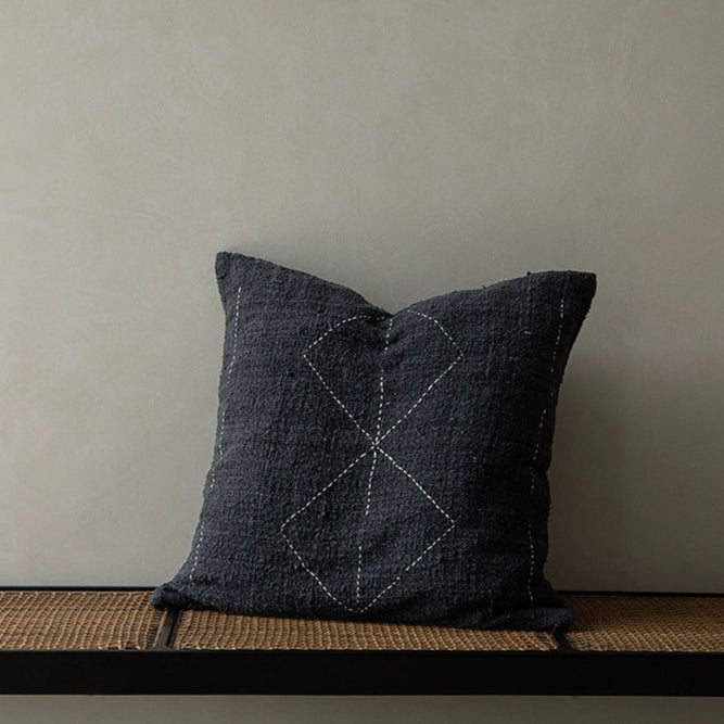 Black Boho throw pillow with white stitching on a woven bench.