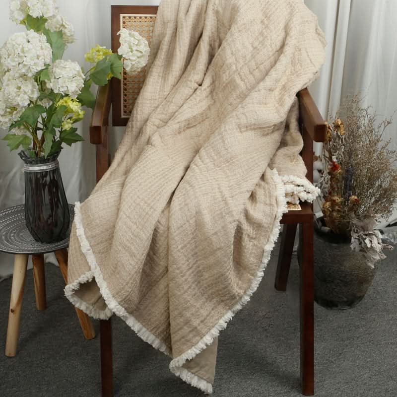 Beige linen cotton throw blanket with tassels draped over a chair, styled with floral decor.