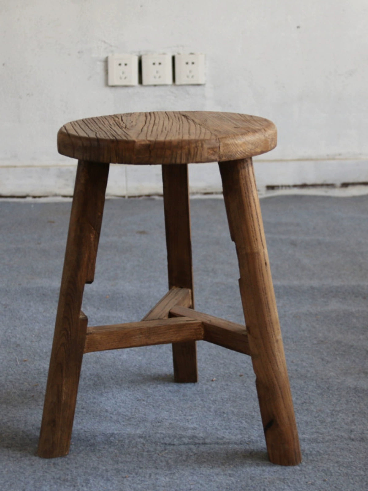 Antique wooden stool, rustic round footstool with Chinese style furniture details on grey carpet.