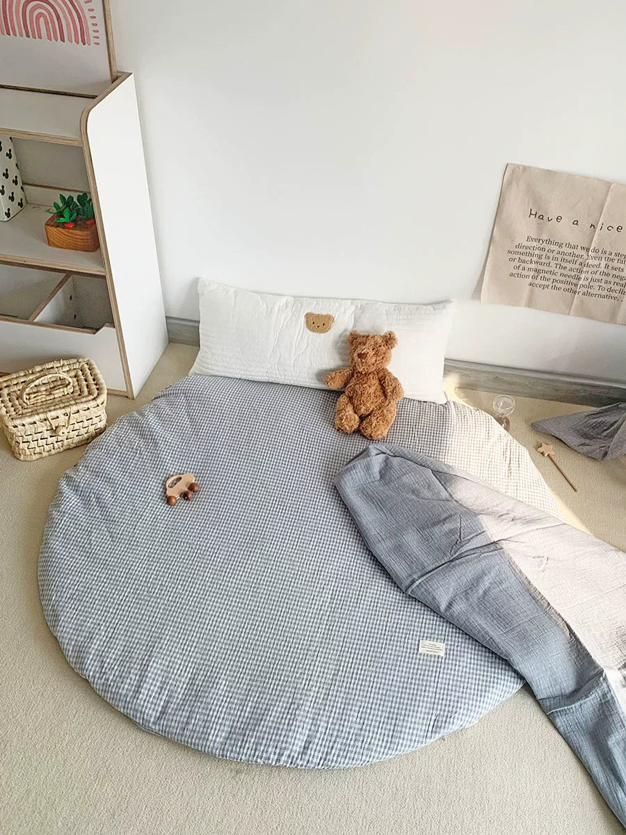 Round baby play mat in light blue and white gingham check pattern with a teddy bear.