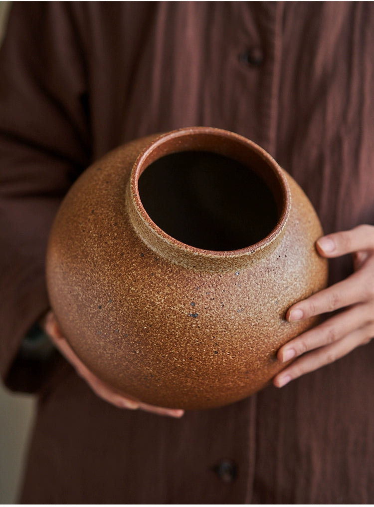 Rustic brown handmade pottery vase, round shape with a textured surface.  Hand-held, showing off the unique glaze.