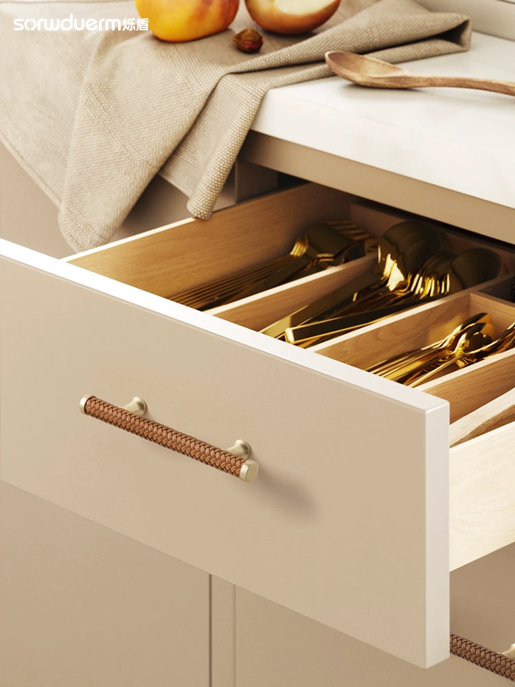 Woven leather drawer pulls, gold finish, modern handles on a cream cabinet drawer.