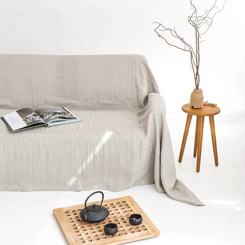 Beige linen sofa throw blanket styled with book, teapot, and wooden side table.