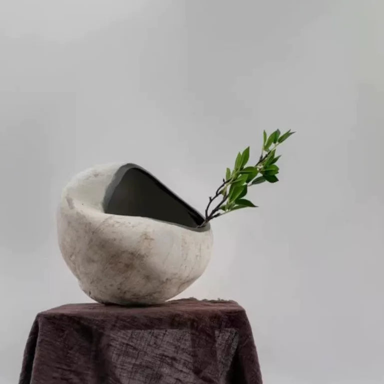 A handmade ceramic vase with a unique sculptural, folded design in a neutral beige finish.