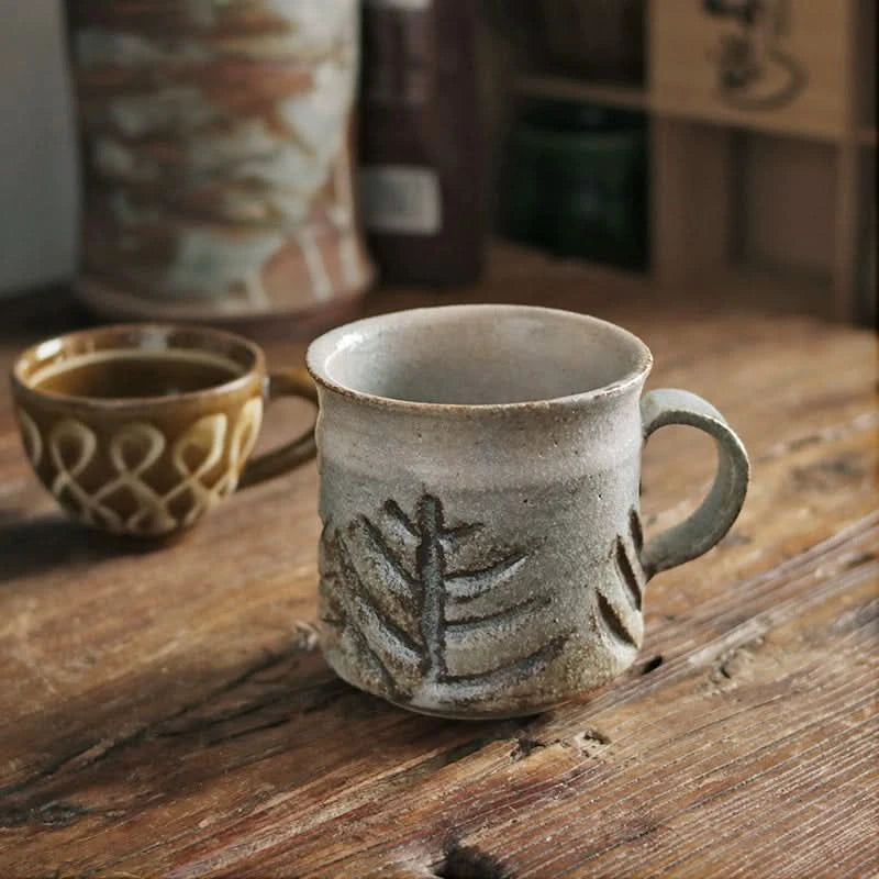 Handmade ceramic coffee mug with rustic tree design, vintage style drinkware on wooden table.