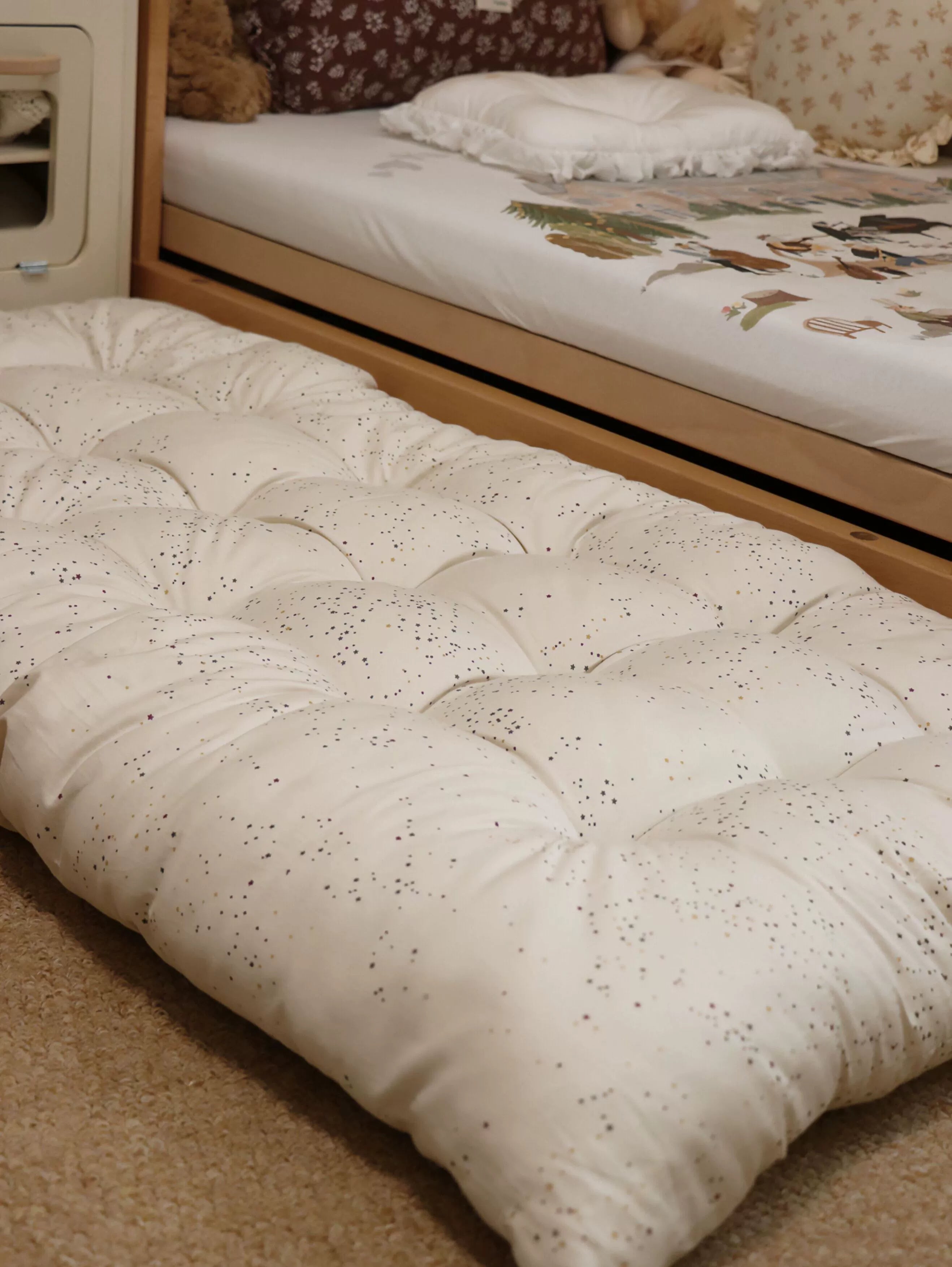 Beige dotted floor cushion with tassels, kids play mat on carpet beside bed.