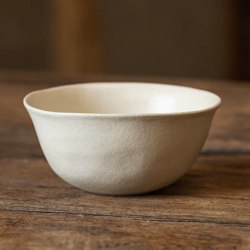 Close-up of a deep, textured, creamy white ceramic bowl with a wide rim on a dark wooden background.