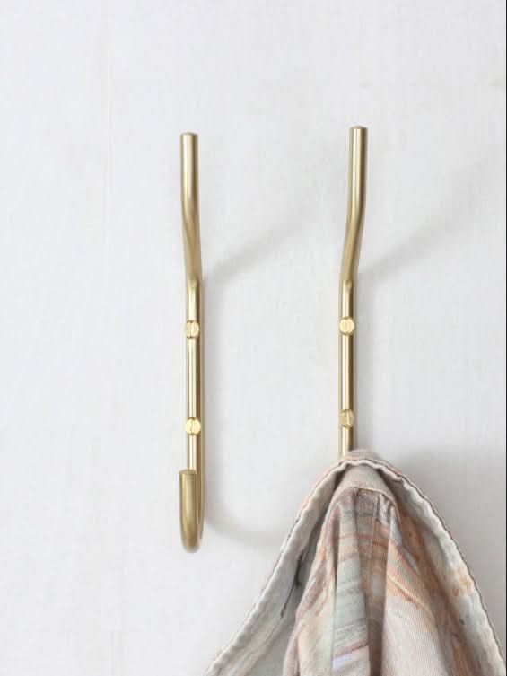 Minimalist brass wall hooks with a garment hanging on one, on a white wall.