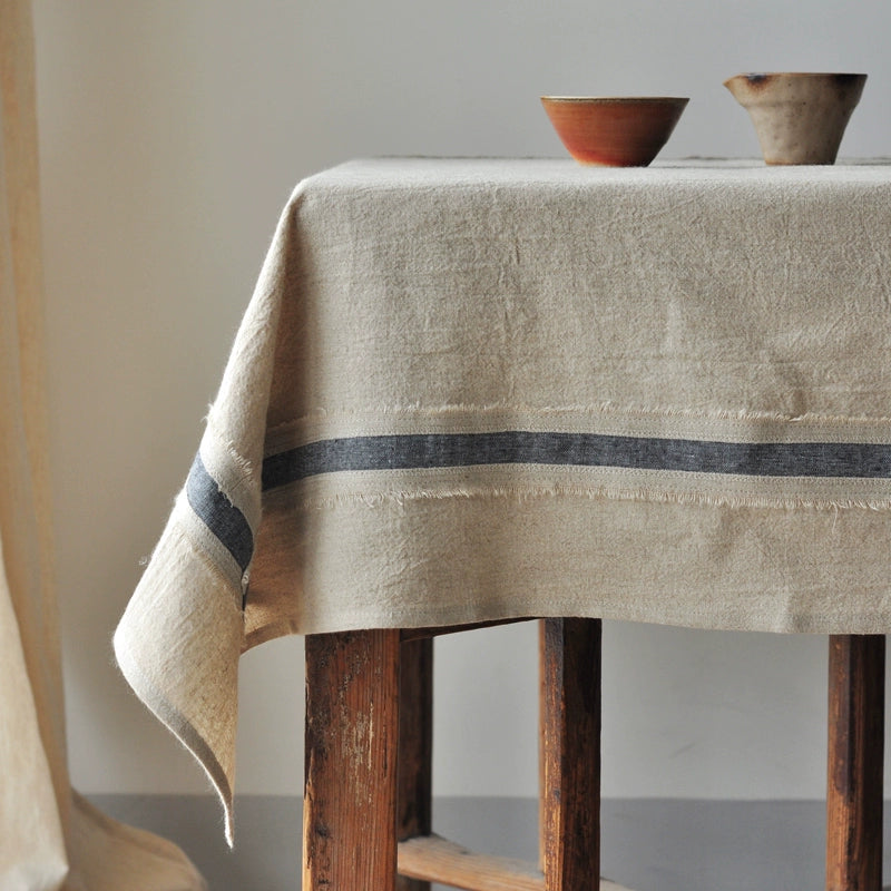 Rustic linen tablecloth with blue striped border draped over wooden table.