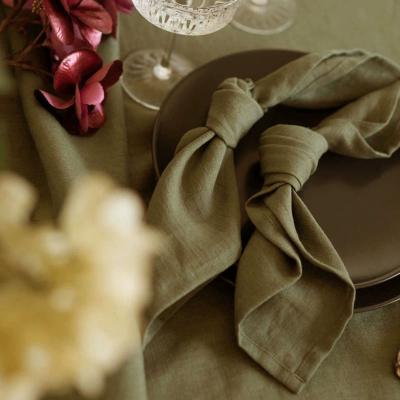 Elegant linen table napkins in olive green, knotted on a plate with floral accents.