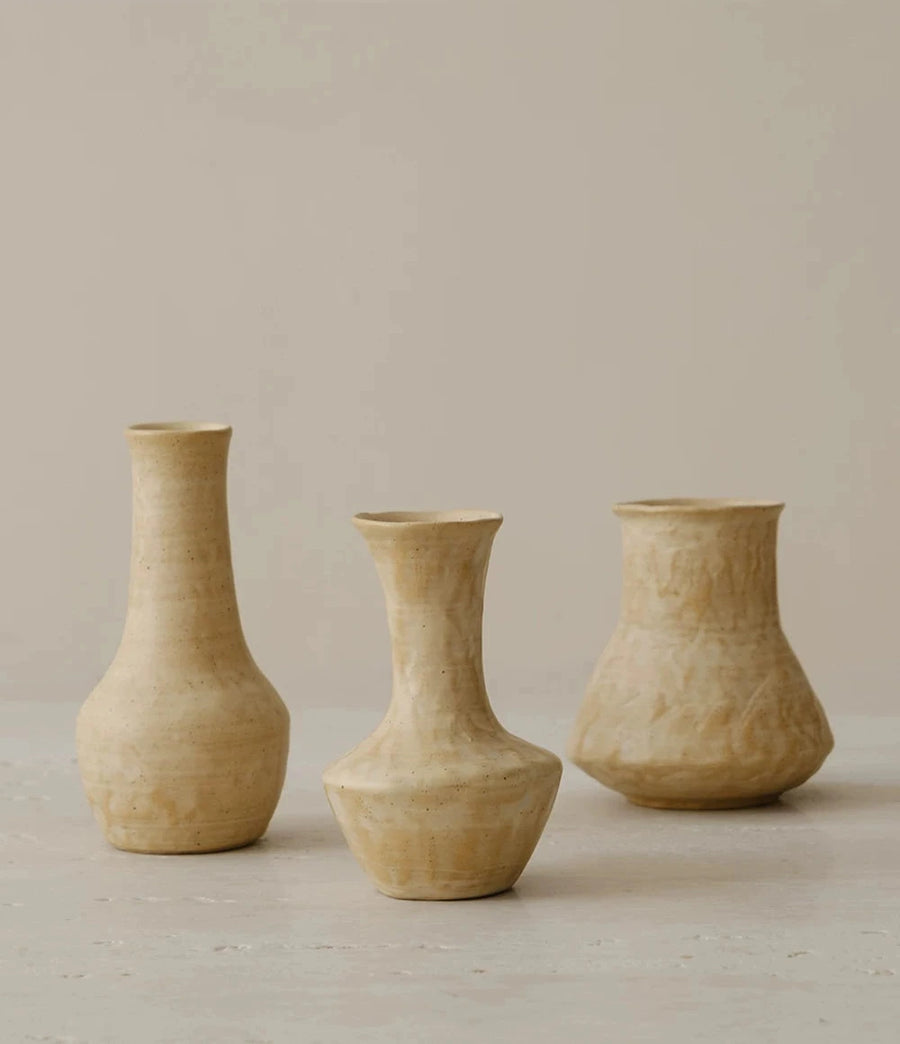 A small, hand-thrown ceramic vase with a textured, creamy white glaze.