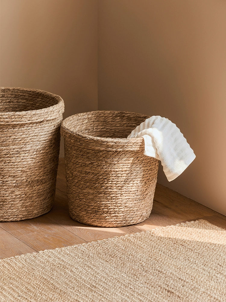 Natural rattan storage baskets in a warm, earthy setting, one holding a white towel.
