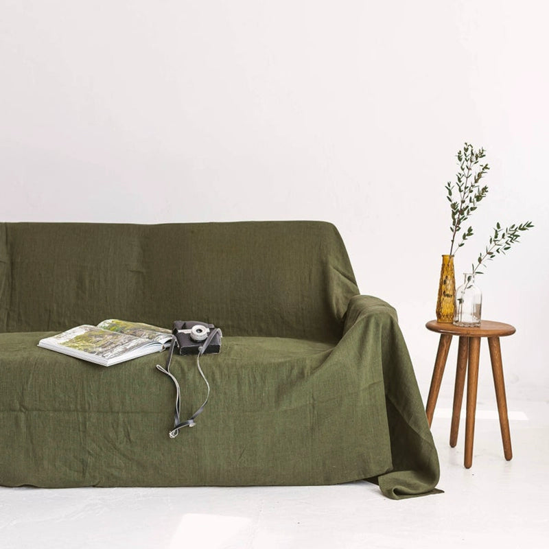 Olive green linen throw blanket draped over sofa, with magazine & camera.