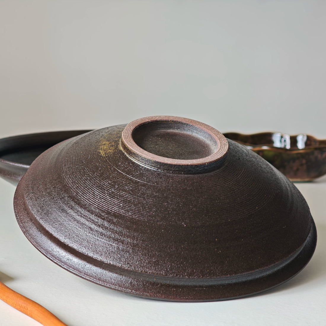 Bottom view of a dark brown ceramic bowl showing the foot ring and textured glazed exterior.