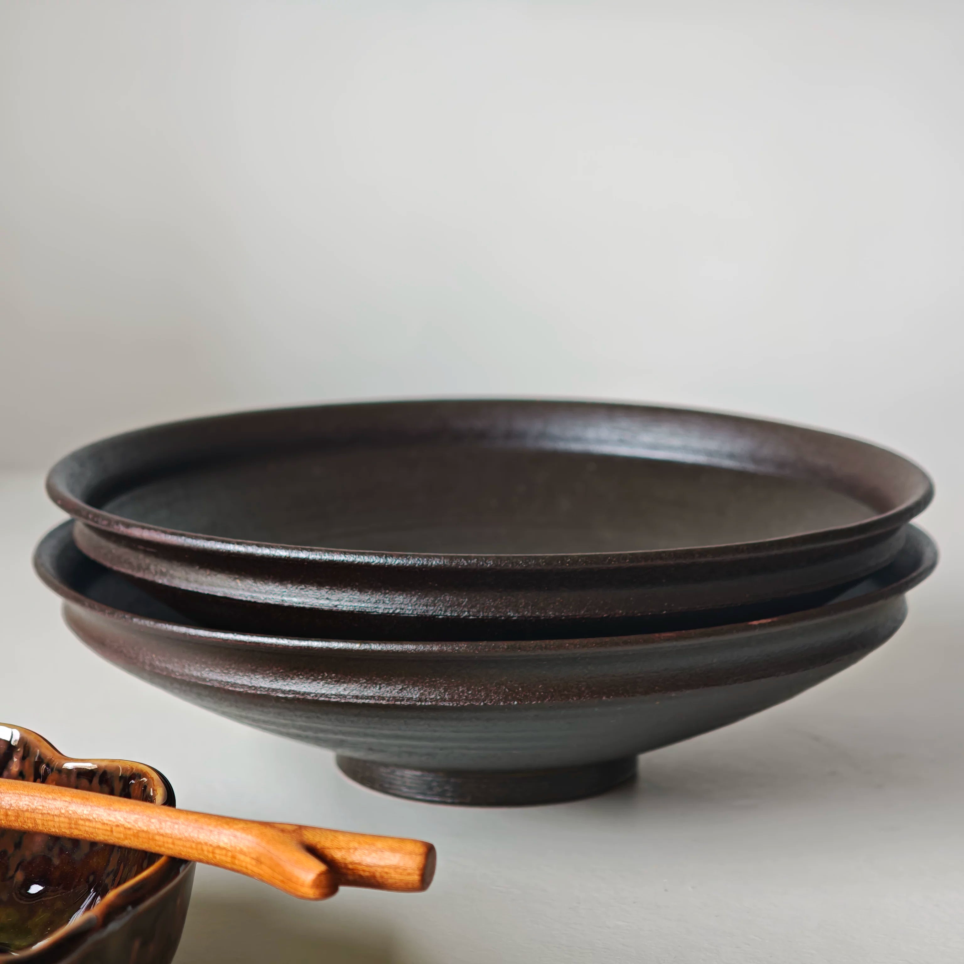 Two dark brown rustic ceramic bowls stacked together on a minimalist studio surface.