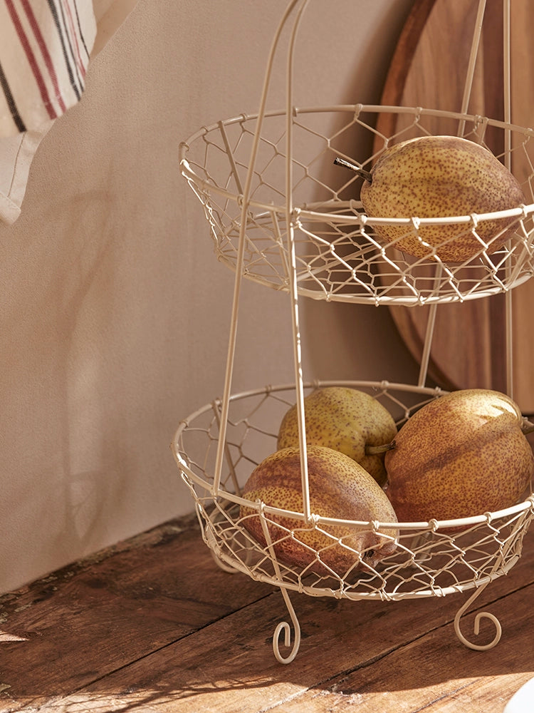 Two-tiered cream-colored wire fruit basket stand with wooden handle.  Rustic design, perfect for displaying fruits and vegetables.