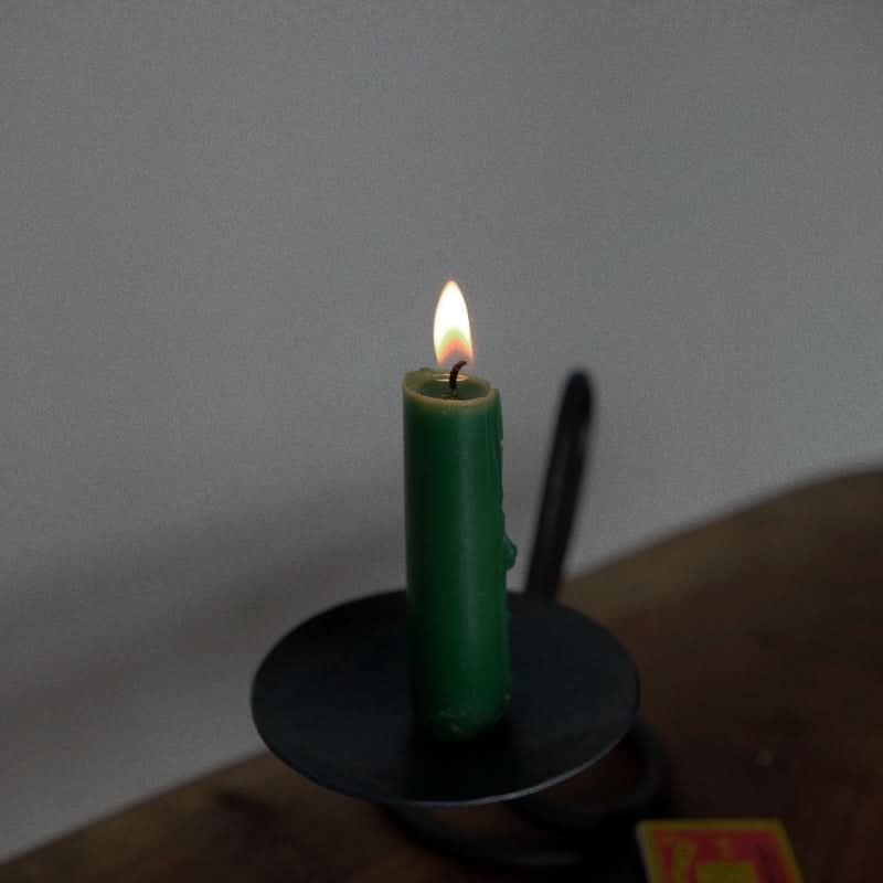 Stylish black candle holder with a lit green candle on a wooden surface.