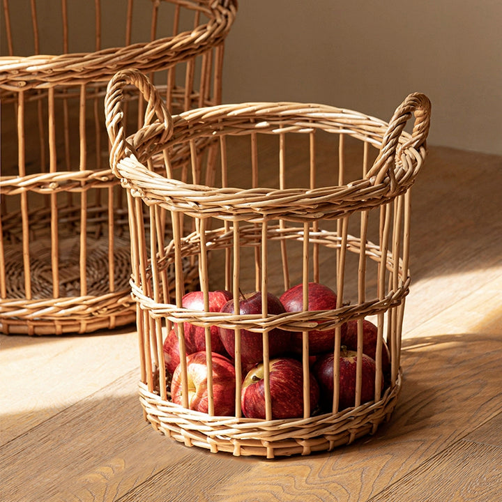 Round woven wicker basket with handles, light beige color.  Filled with red apples.  Natural rattan material.  Stylish storage basket for fruits, vegetables, or decor.
