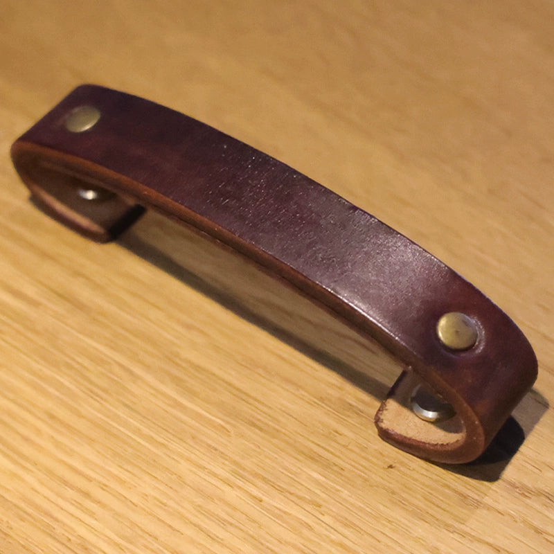 Brown leather drawer pulls with brass accents on a wooden surface. Rustic cabinet handles.