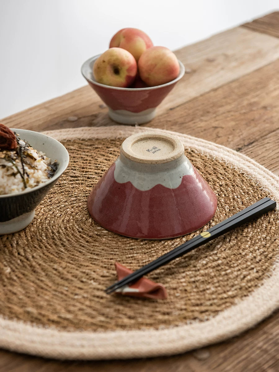 Inverted dusty pink ceramic bowl resting on a woven placemat with peaches nearby.