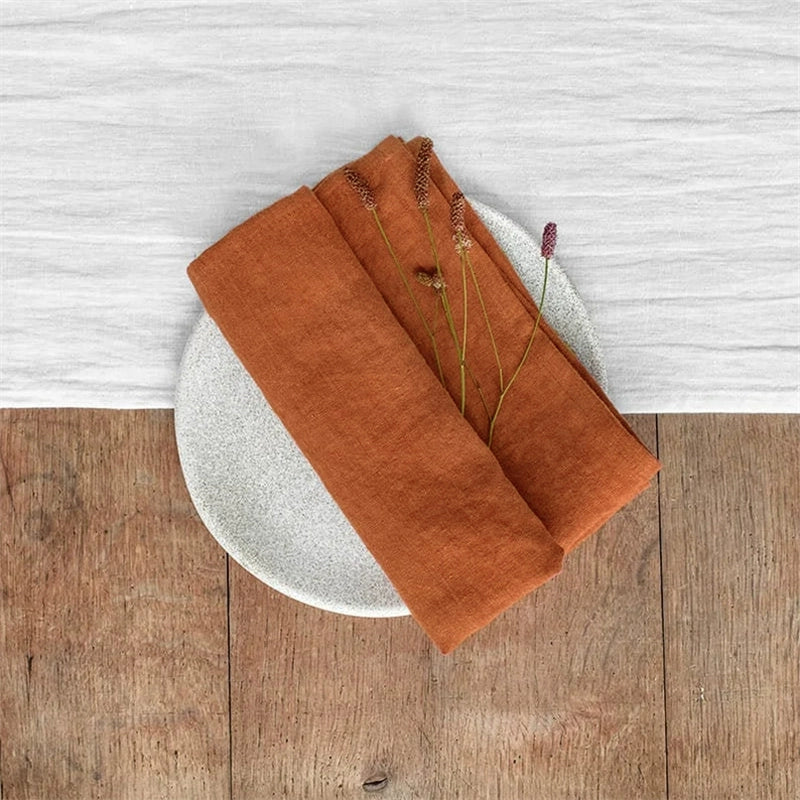Terracotta linen table napkins, knotted, set of 4, with dried floral accent on plate.
