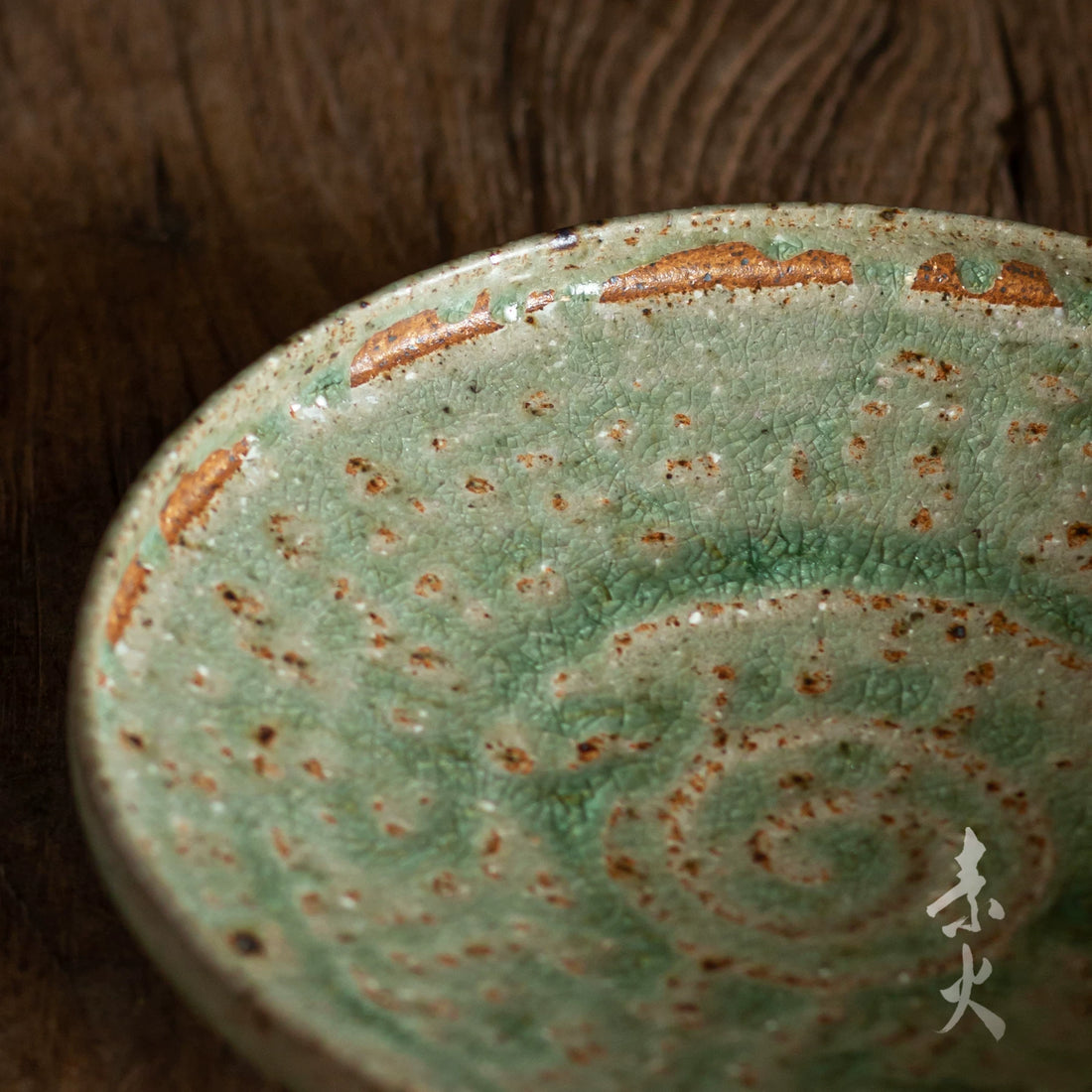 Close-up of a handmade ceramic dish with a vibrant, crackled green glaze and brown undertones.