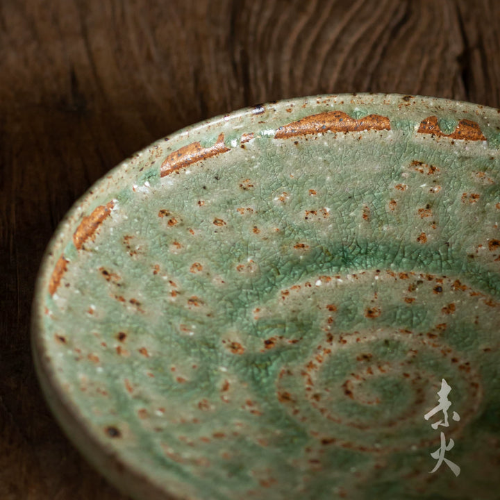 Close-up of a handmade ceramic dish with a vibrant, crackled green glaze and brown undertones.