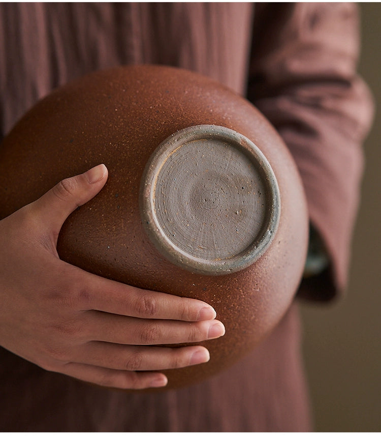 Rustic brown handmade pottery vase, 23cm high, 11cm diameter.  Hand-held, showing textured surface and light gray base.
