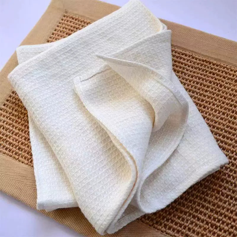 Waffle weave cotton towels, beige, grey, and white, set of 4, folded on a woven placemat.  Soft, textured, and absorbent.