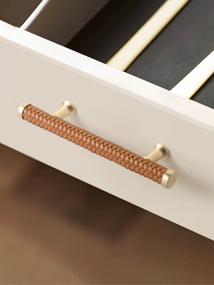 Woven leather drawer pull, gold finish.  Beige braided leather handle on a light beige cabinet.