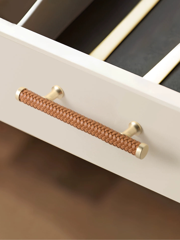 Woven leather drawer pull, gold tone, light beige cabinet.  Braided brown leather handle.