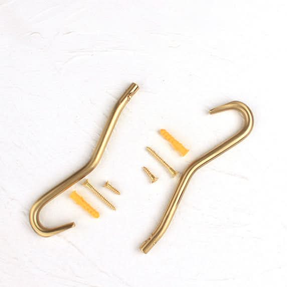 Minimalist brass wall hooks and mounting hardware on a white textured surface.