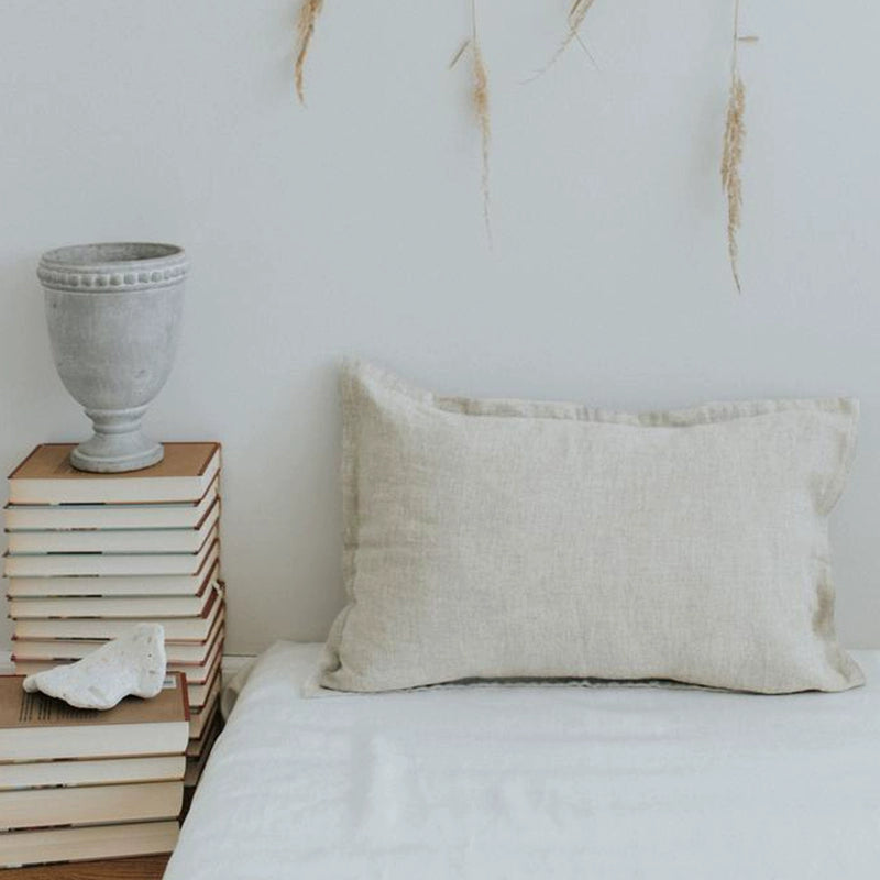 Natural linen pillow case with frills on a white duvet, beside stacked books and decor.