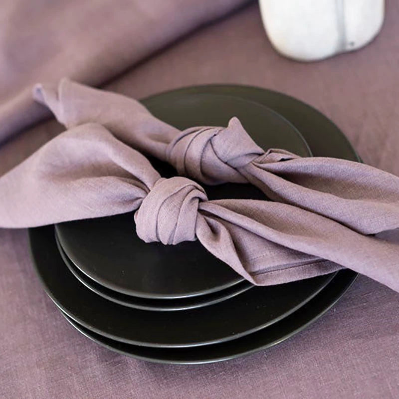 Elegant linen table napkins in mauve, knotted on black plates, set of 4.