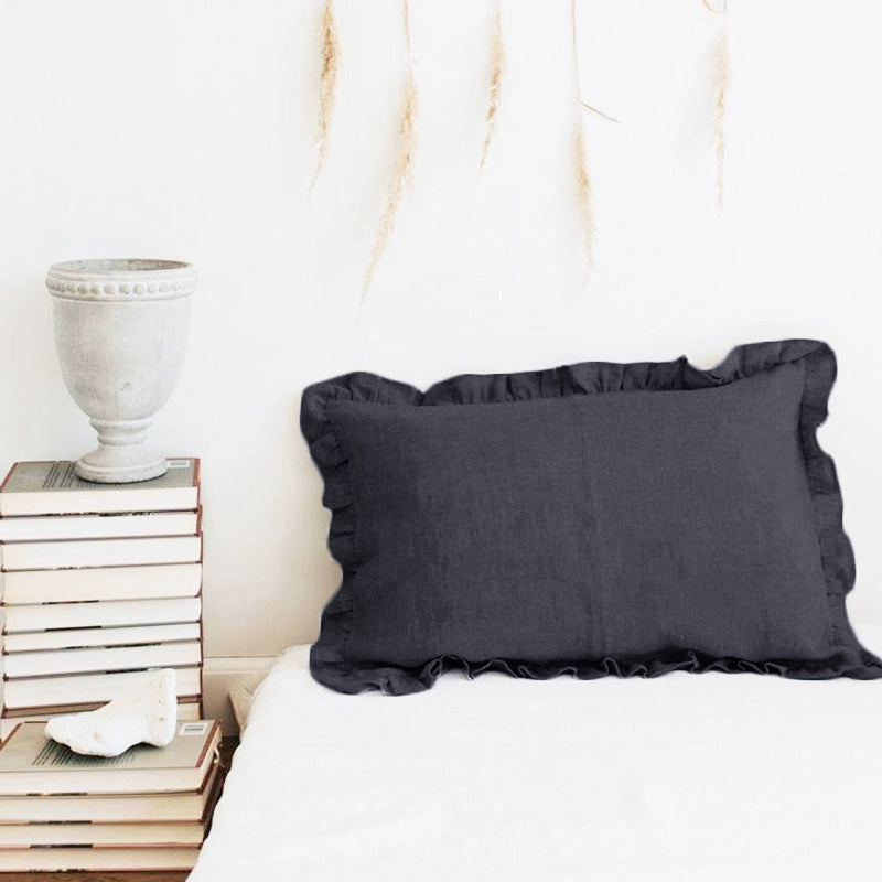 Elegant dark grey linen pillow case with frills on a white bed.