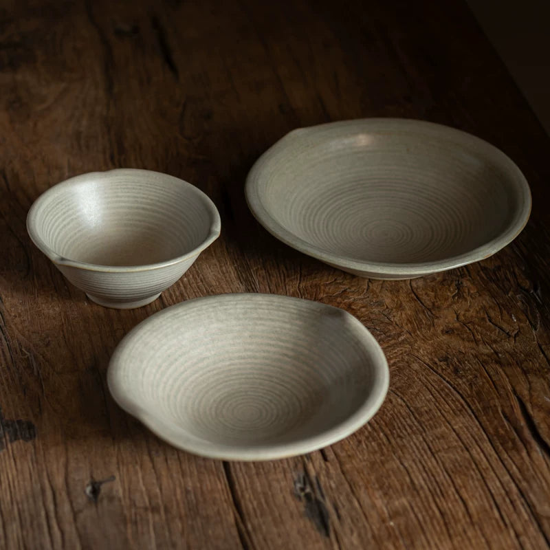 Three light-colored ceramic pieces (small bowl, saucer, medium bowl) on a wooden surface.