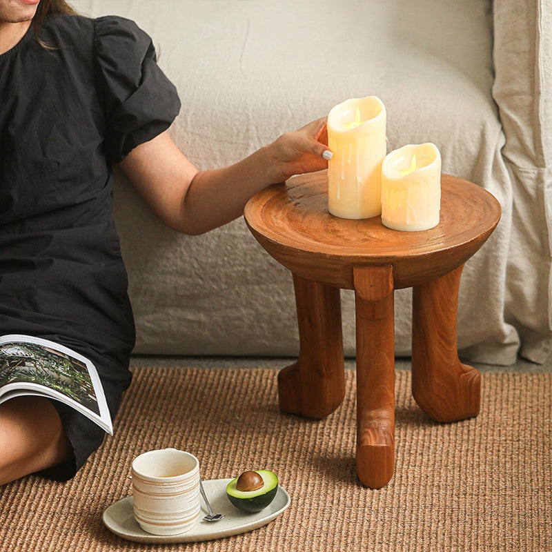 Wooden round side table with curved legs, light brown finish. Two pillar candles on the table.  Stylish accent piece.